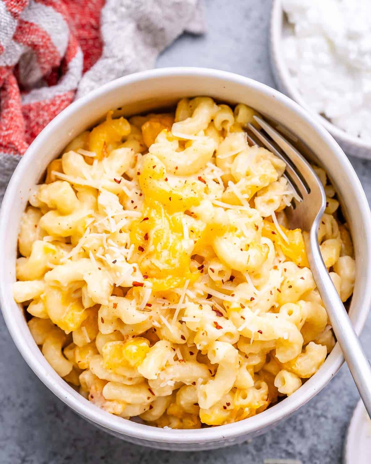 Bowl of mac and cheese garnished with black pepper and chili flakes, with a fork ready to eat.