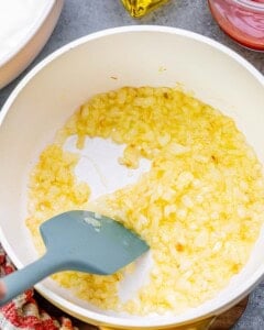 Sautéed diced onions in olive oil cooking in a pan until soft and golden.
