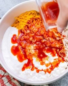 Ingredients including shredded chicken, shredded cheddar, Greek yogurt, and buffalo sauce being added to the bowl.
