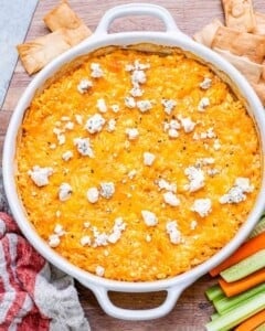 Baked buffalo chicken dip in a white baking dish, golden on top and sprinkled with crumbled blue cheese.