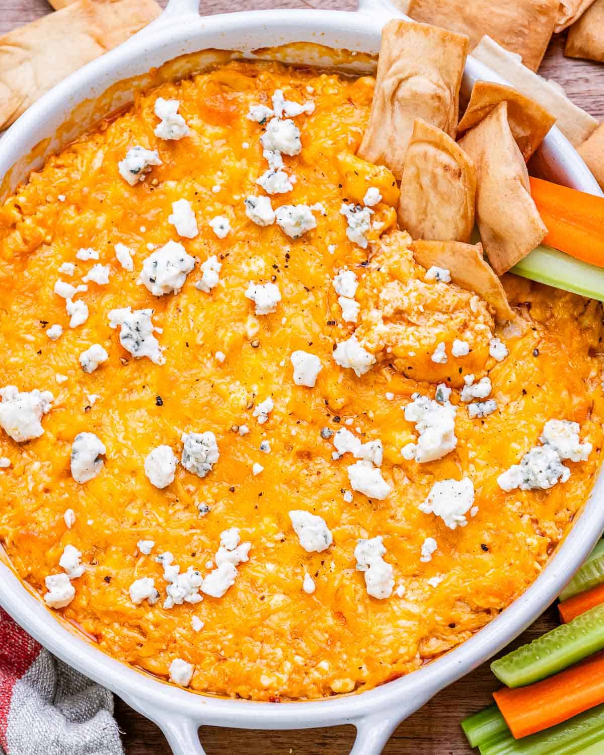 Close-up of the buffalo chicken dip with pita chips and celery sticks on the side, showing the melted cheese and blue cheese topping.