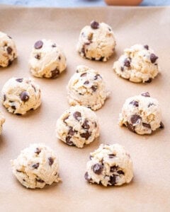 Cookie dough scooped into round balls with chocolate chips, arranged on a parchment-lined baking sheet.