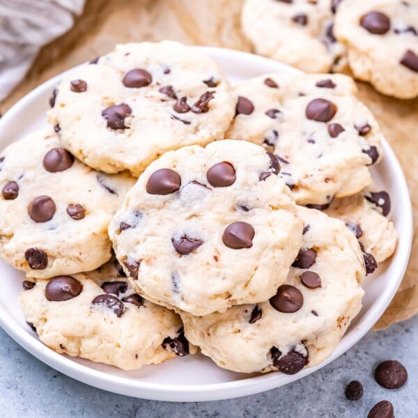 Pile of cookies on a round plate with more chocolate chips scattered on top and around.