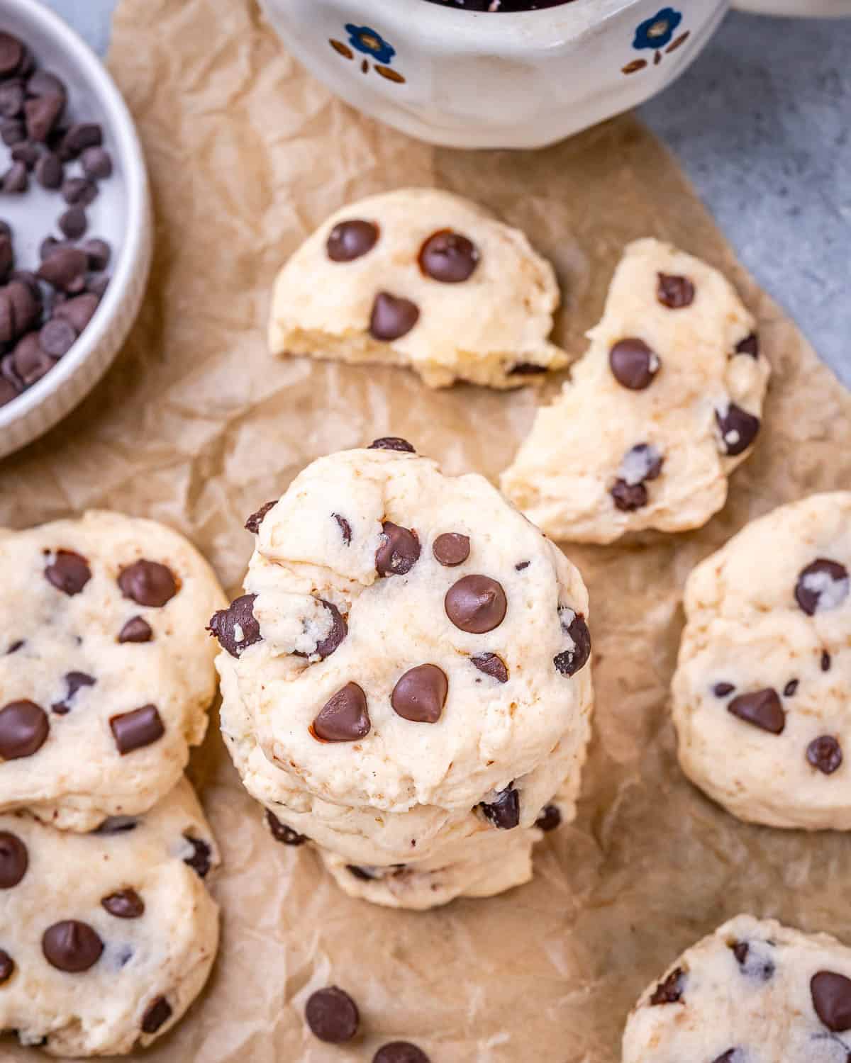 Baked cottage cheese chocolate chip cookies stacked on parchment paper with melted chocolate chips on top.