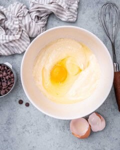 Wet mixture blended until smooth in a mixing bowl with cracked egg and whisk beside it.