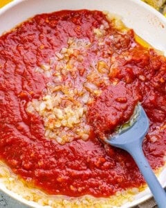 adding marinara sauce to sauteed onions and garlic to make tomato sauce