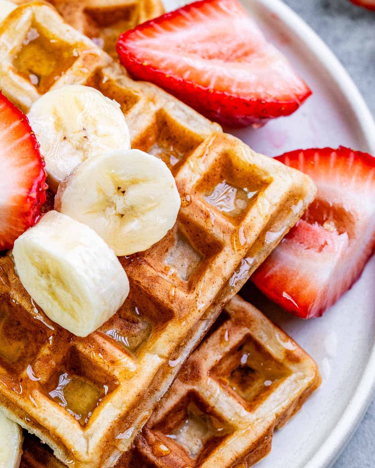 Waffles on a plate topped with fruits. 