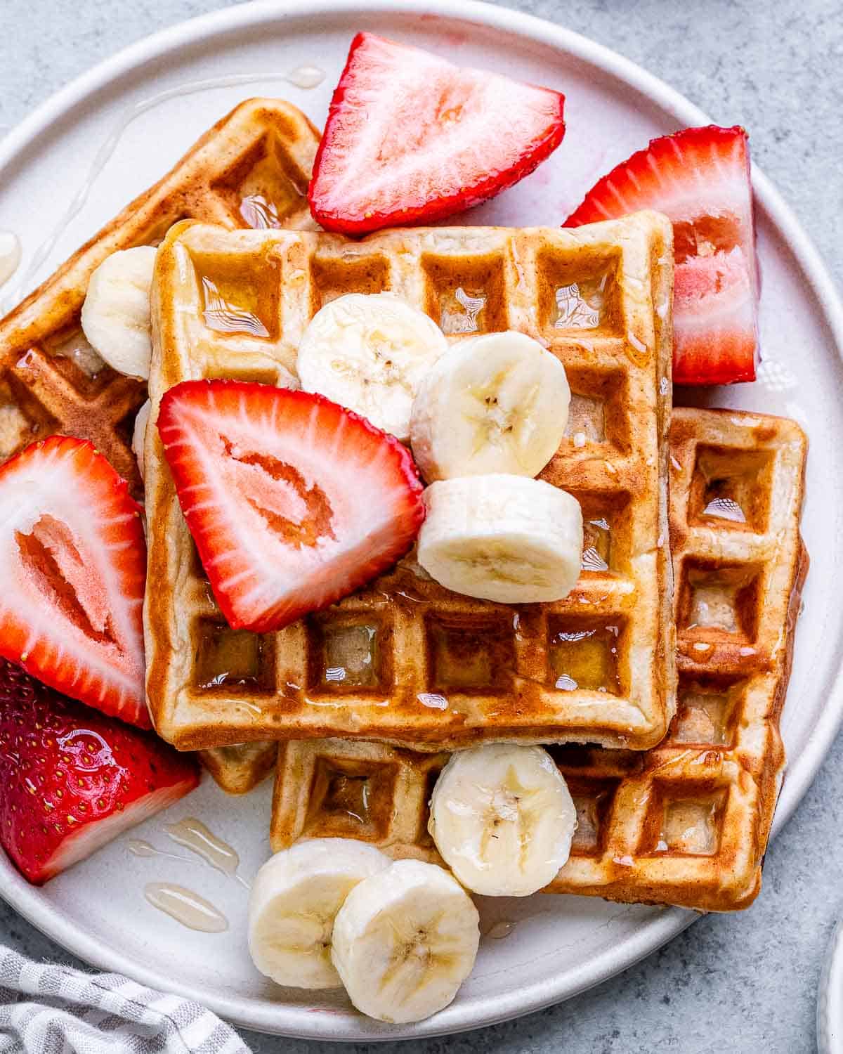 Waffles on a plate topped with strawberries and bananas.