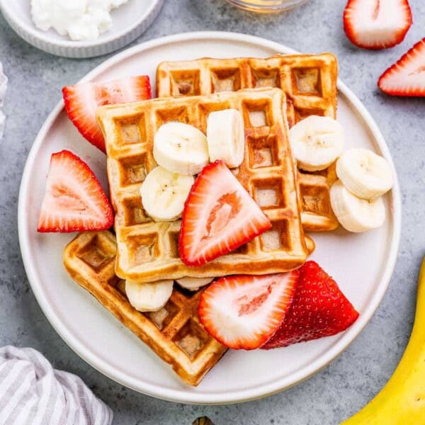 waffles on a plate topped with slices of strawberries ans bananas.