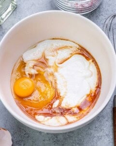 Greek yogurt, egg, vanilla, and honey in a bowl before being whisked together.