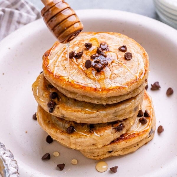 Side angle of Greek yogurt pancakes with honey being drizzled from a dipper.