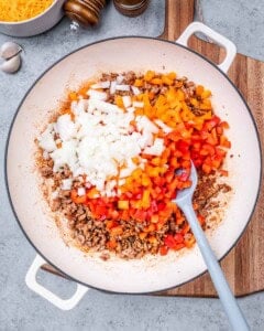 Chopped red and yellow bell peppers with diced onions being added to the cooked ground turkey in the skillet.