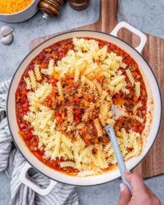 Cooked pasta being folded into the skillet with the sauce and meat.