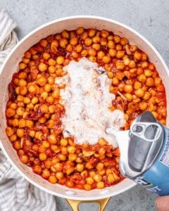 Coconut cream poured over chickpeas and tomato sauce in a pan.