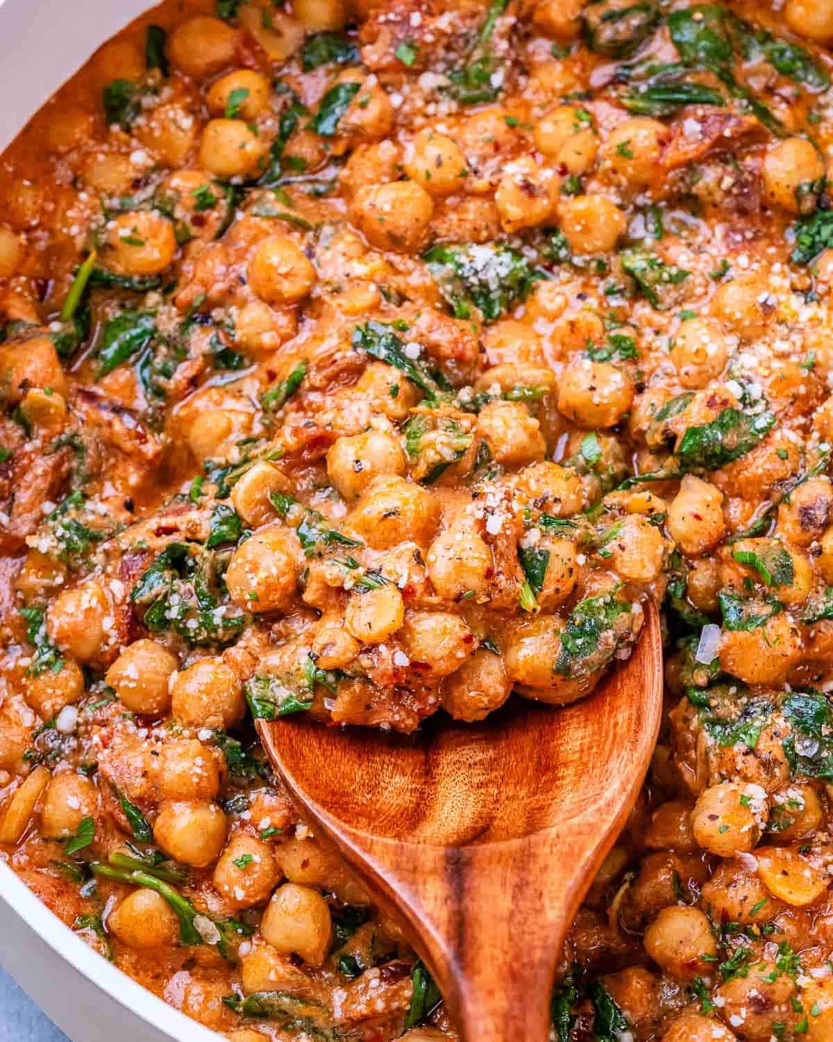Close-up of creamy Marry Me Chickpeas with spinach and Parmesan, stirred together in a skillet.