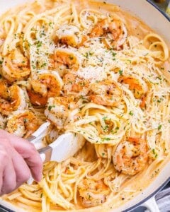 Tongs lifting a shrimp from the pasta to show detail and texture.