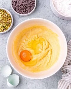 A mixing bowl with the creamed butter and sugar mixture, and one cracked egg added on top, ready to be mixed in.