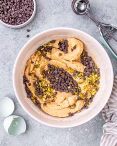 Cookie dough in a mixing bowl, now mixed and topped with mini chocolate chips and finely chopped roasted pistachios.