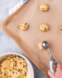 Cookie dough balls scooped and spaced out on a parchment-lined baking sheet, ready to be baked.