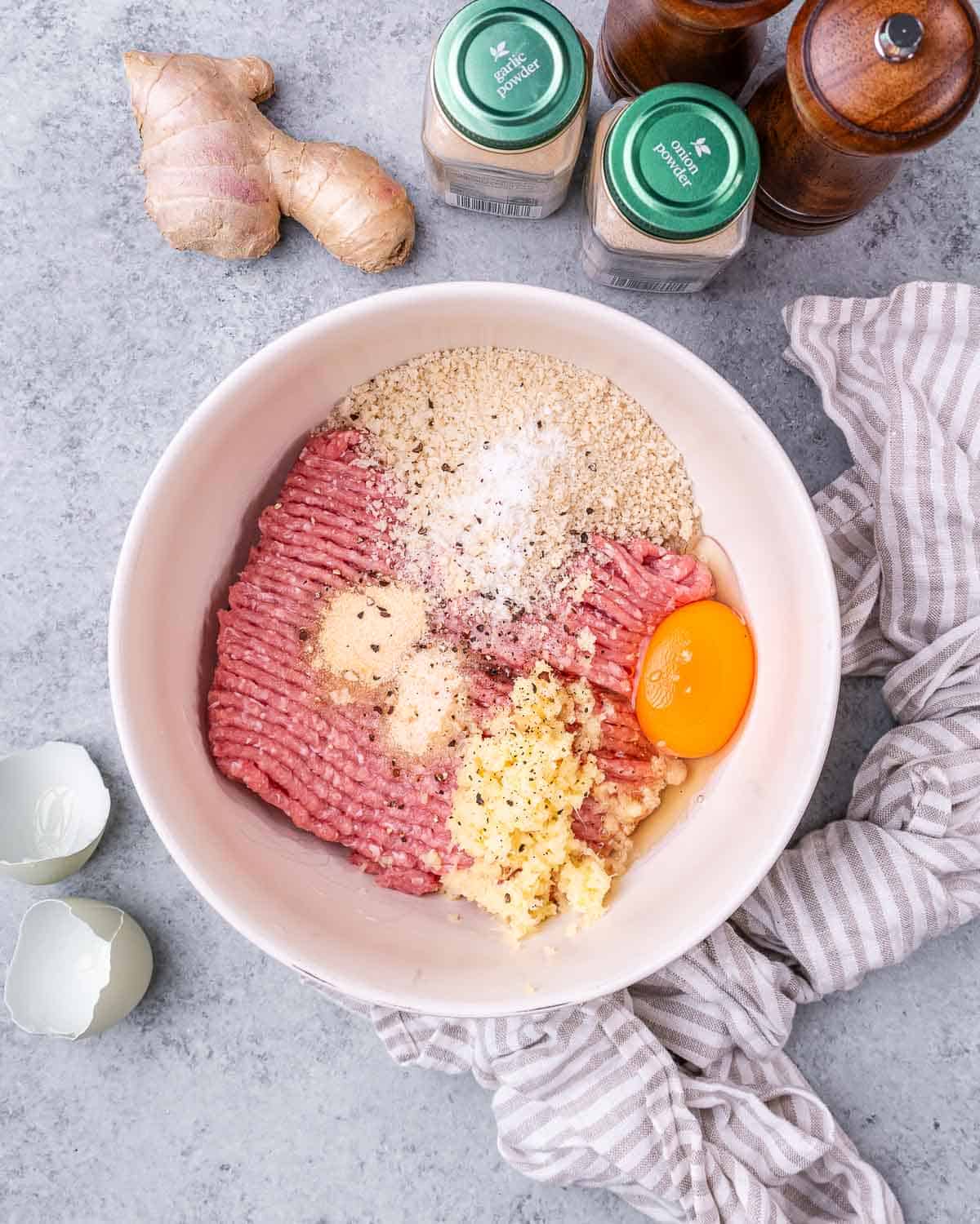 Ground turkey, spices, breadcrumbs, and an egg in a white bowl.