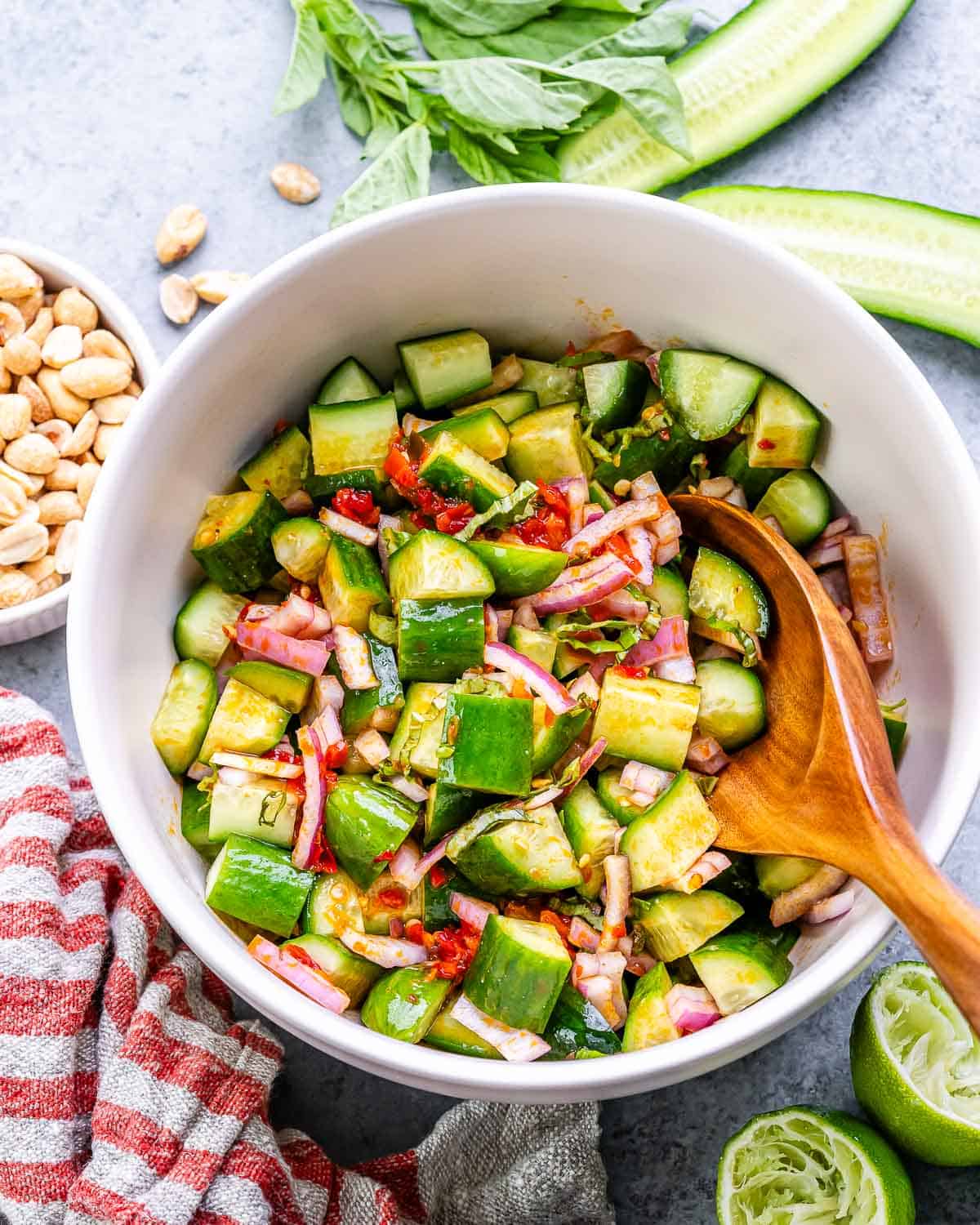 Asian cucumber salad in a white bowl with a wooden serving spoon