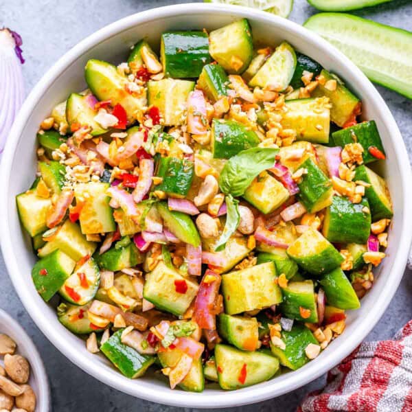 a round white bowl with cucumber salad with Thai dressing.