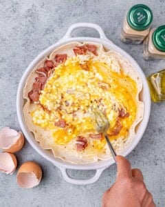 Scrambling eggs and ingredients in a white dish with a fork.