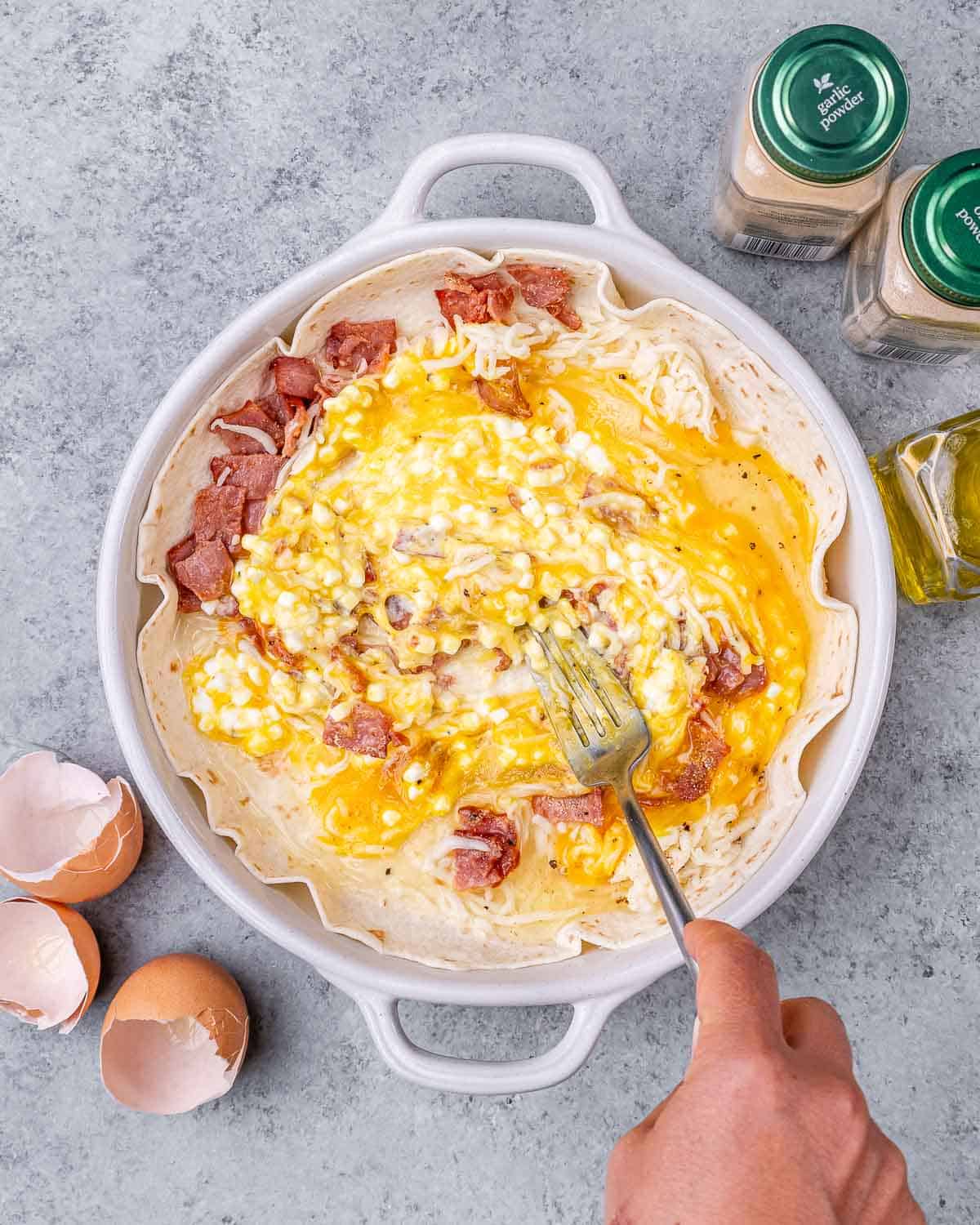 Scrambling eggs and ingredients in a white dish with a fork.