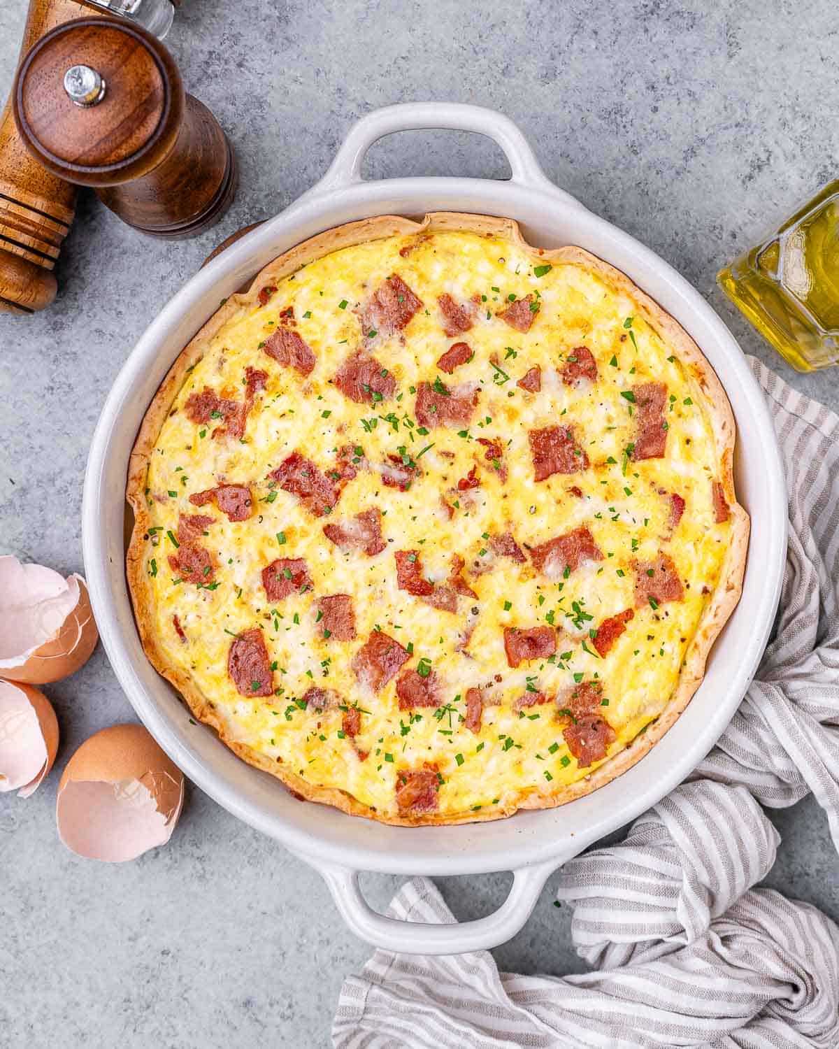 A quiche with bacon and cheese in a white dish.