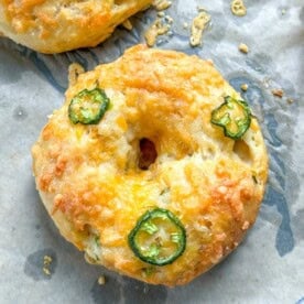 a single bagel on a pan, topped with cheese and sliced jalapenos.