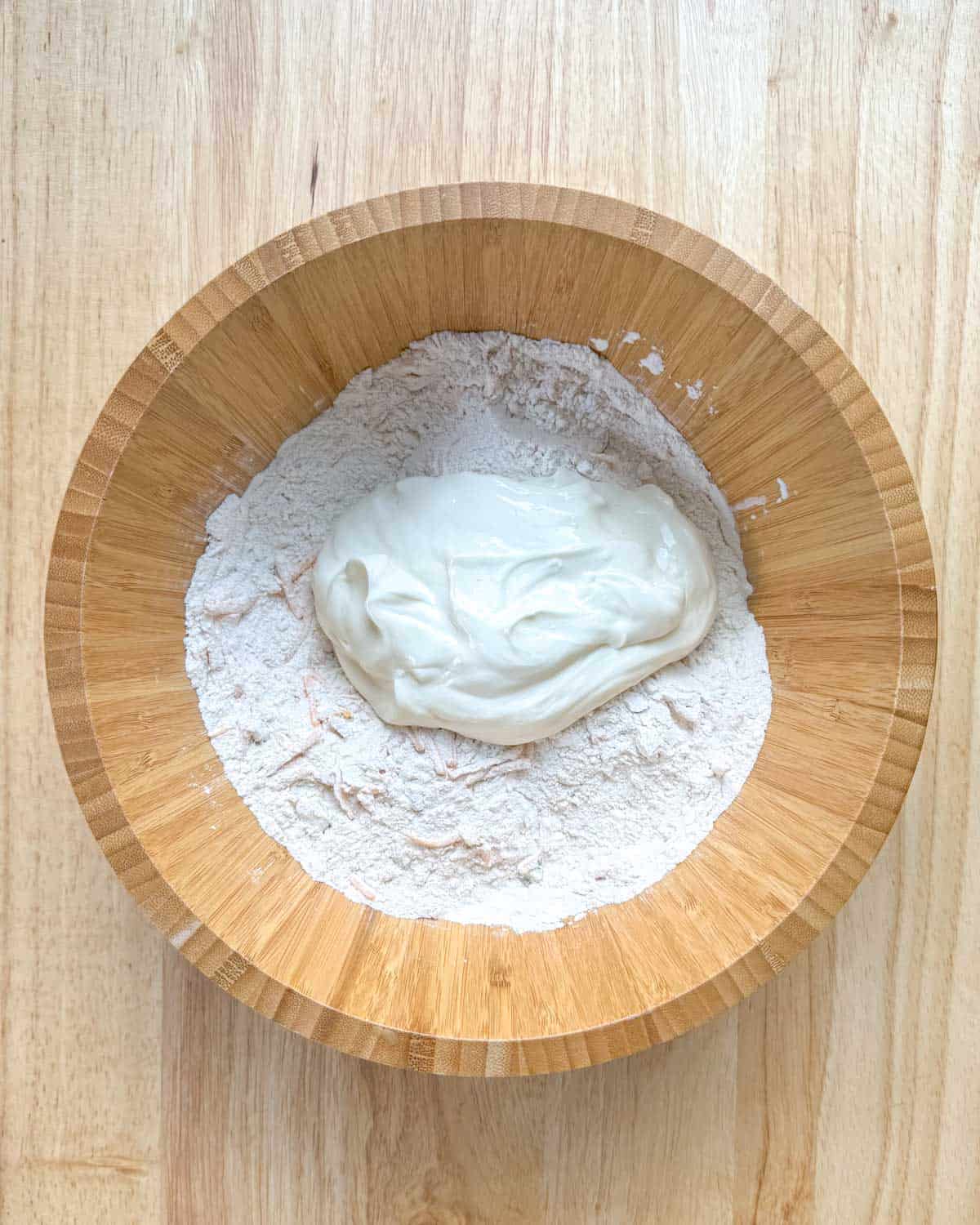Zesty Jalapeno Cheddar Bagels 13 Greek yogurt being added to the flour and cheese mixture in a bowl.