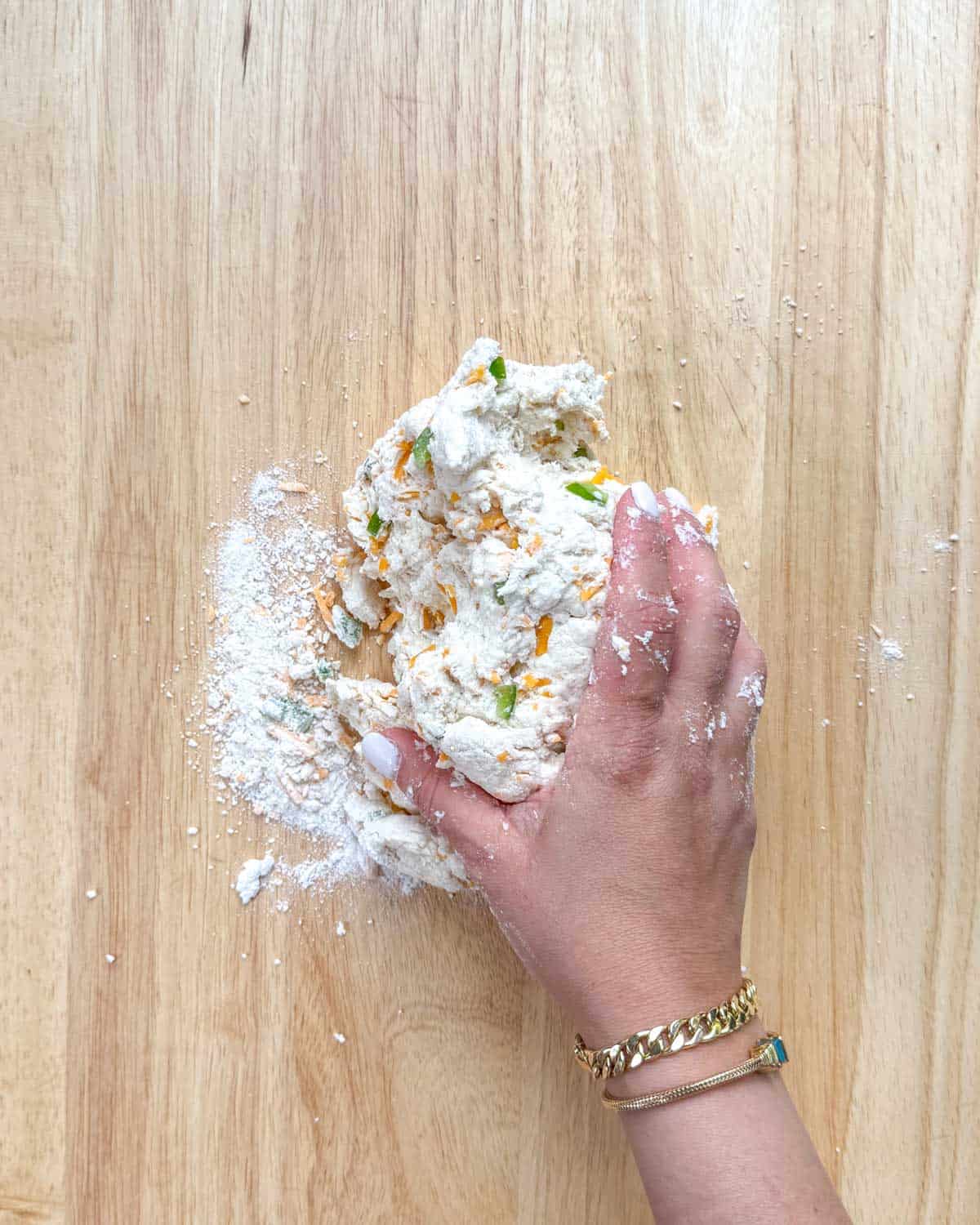 Zesty Jalapeno Cheddar Bagels 14 A hand kneading bagel dough on a cutting board dusted with flour.