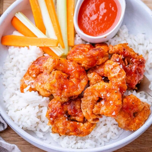 A bowl of rice topped with buffalo shrimp.