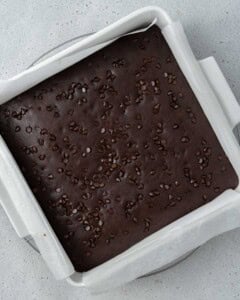 Overhead view of baked brownies in a parchment-lined pan with chocolate chips scattered across the surface.