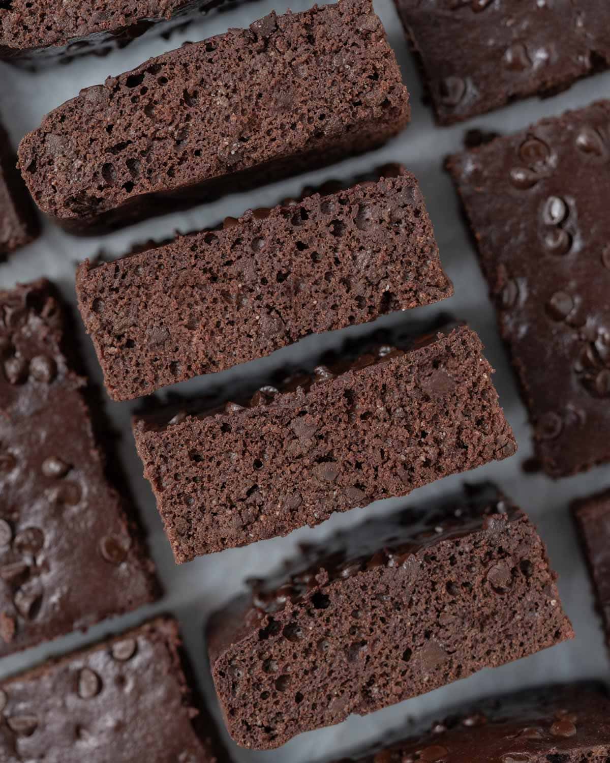 Rows of evenly cut brownies topped with melted chocolate chips, arranged neatly on parchment.