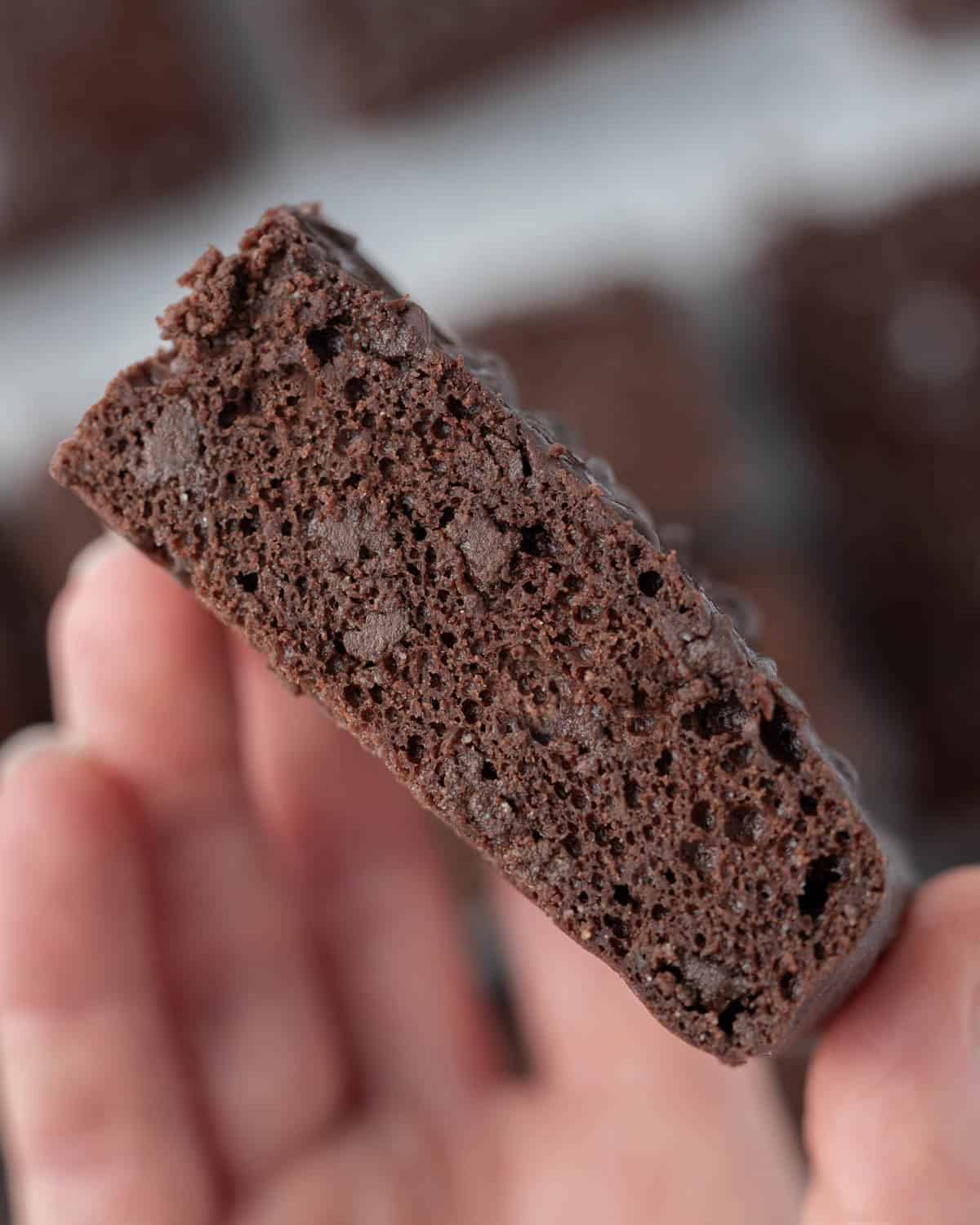 A side view of a brownie piece being held up close, showing its airy yet rich crumb.