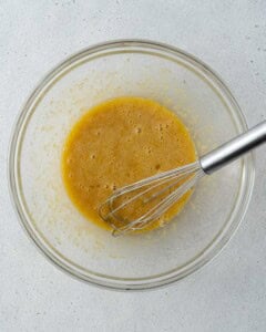 Eggs, sugar, and vanilla extract whisked together in a glass bowl with a whisk in it.