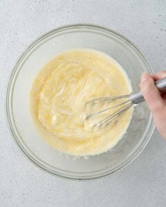 Wet ingredients and yogurt being mixed together with a whisk in a glass bowl.
