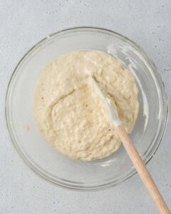 Muffin batter being gently mixed with a spatula in a glass bowl.