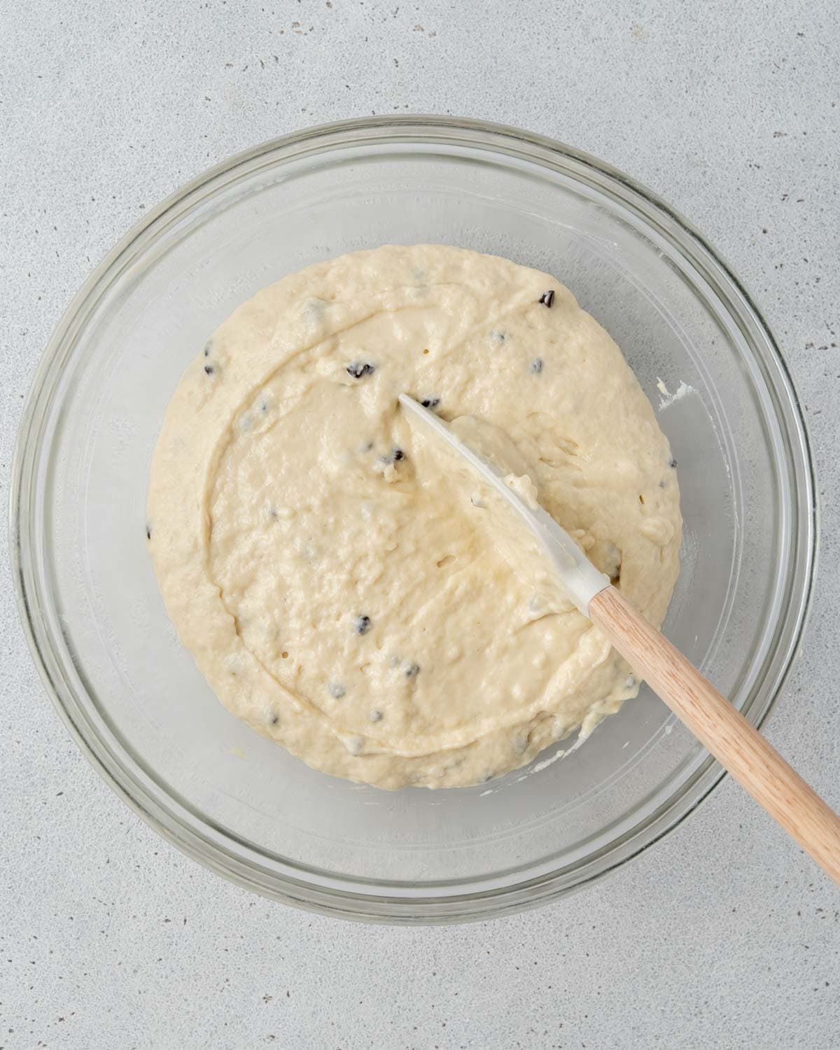 Top view of glass bowl with muffin batter being mixed with chocolate chips in it.