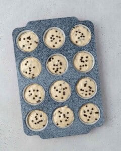 Muffin tin filled with raw batter, each cup topped with a few chocolate chips before baking.