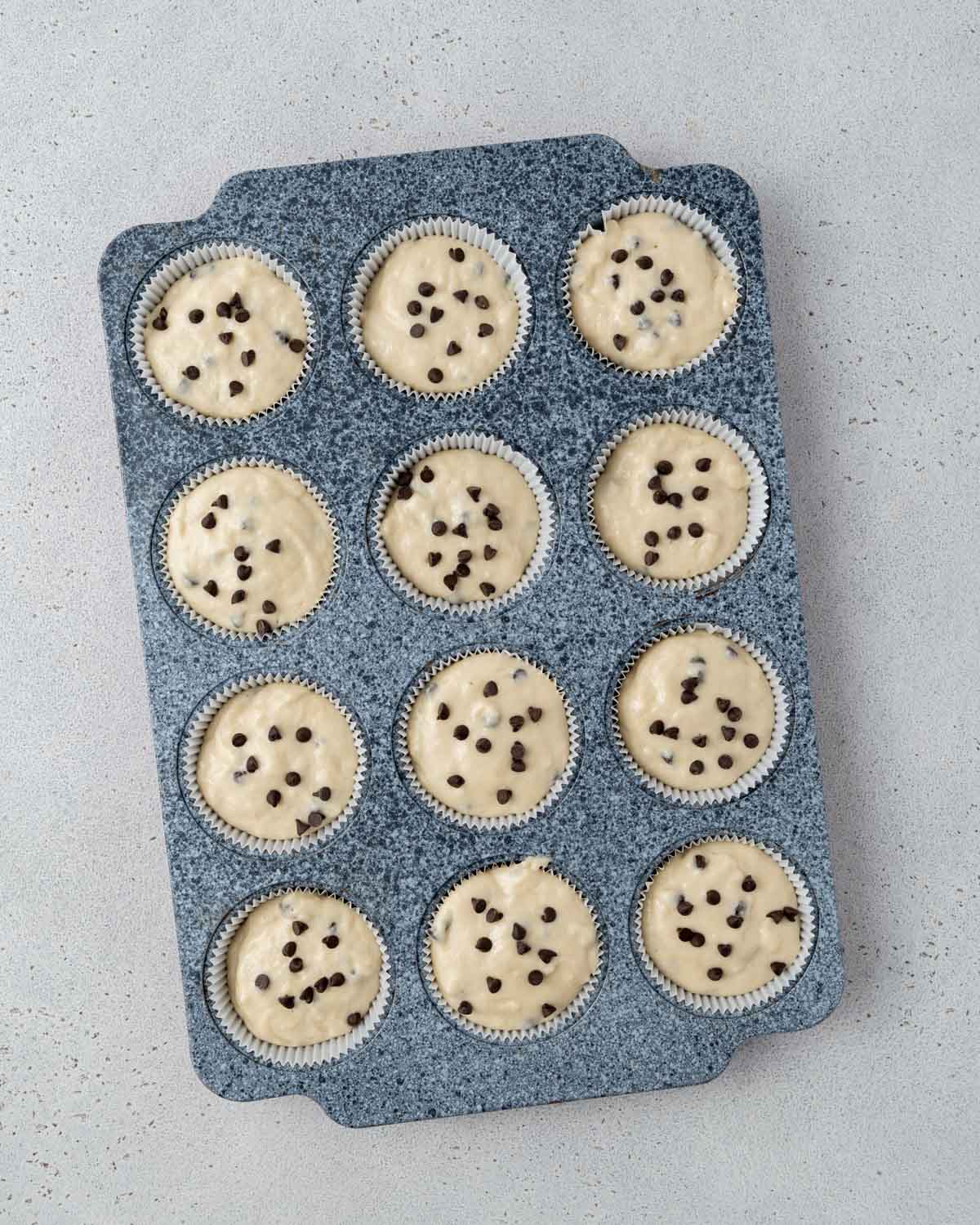 Muffin tin filled with raw batter, each cup topped with a few chocolate chips before baking.