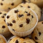Overhead view of two chocolate chip muffins in white liners, stacked slightly to show texture.
