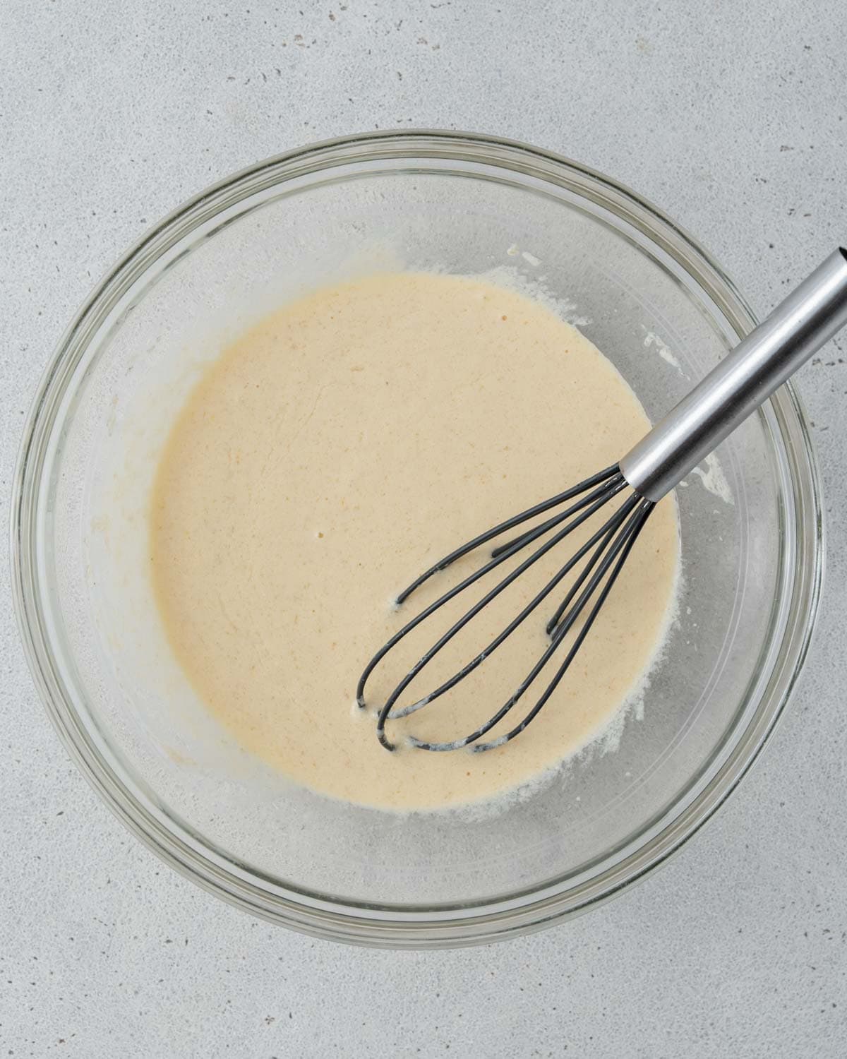 Whisking wet ingredients including yogurt, eggs, vanilla, milk, and sugar in a glass bowl.