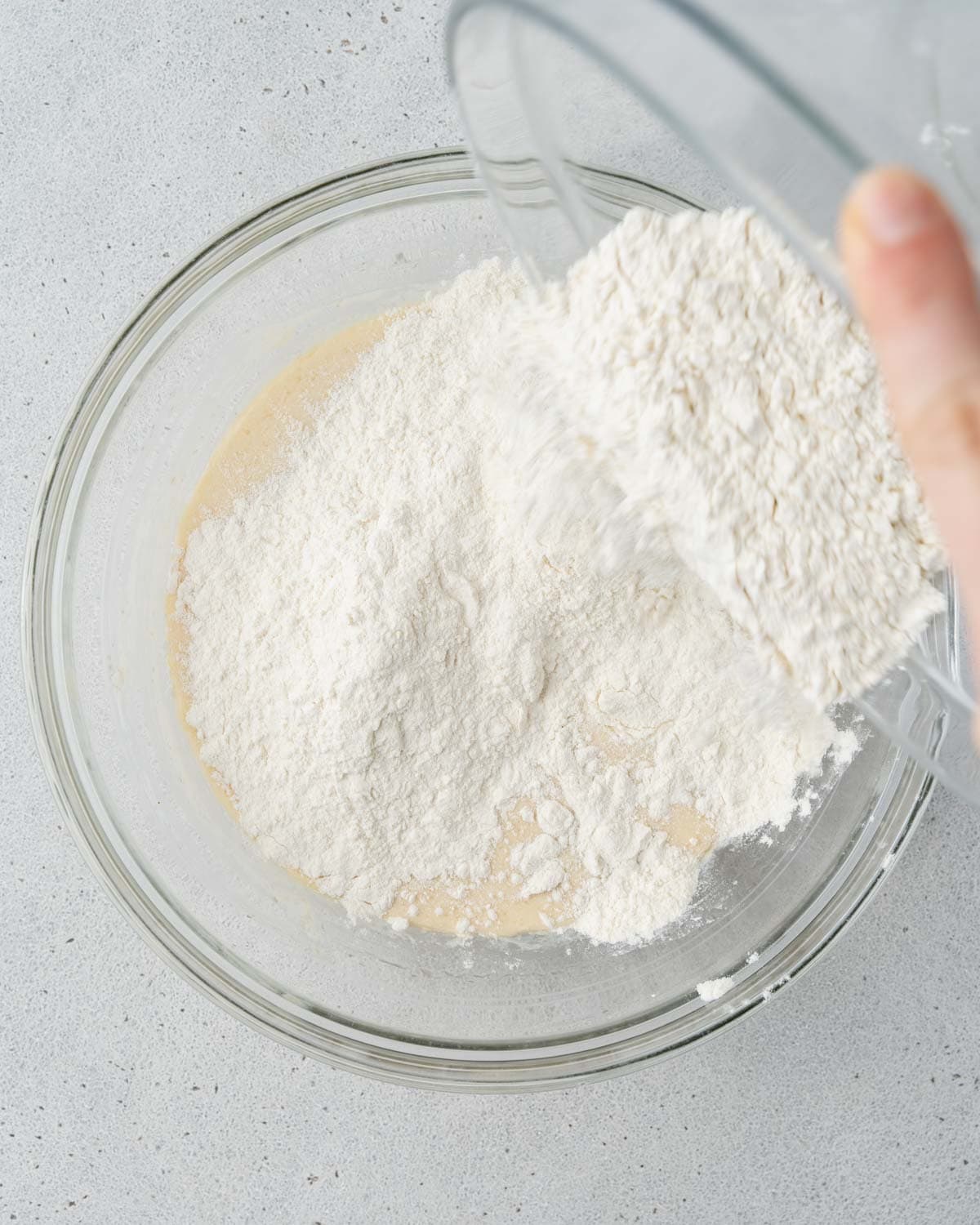 Flour being added to the wet ingredients in a glass mixing bowl.