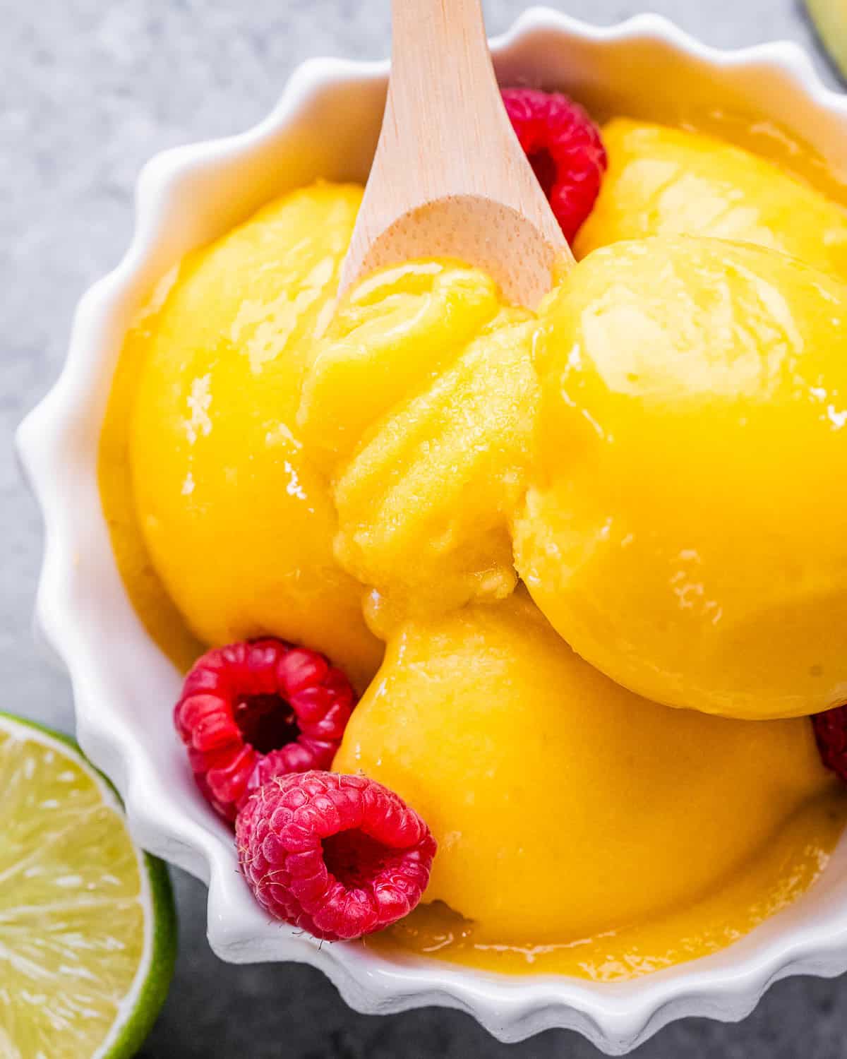 a bowl with 3 scoops of mango sorbet topped with fresh raspberries.