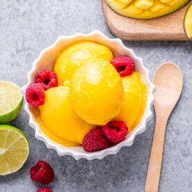 Mango sorbet in a bowl topped with raspberries.
