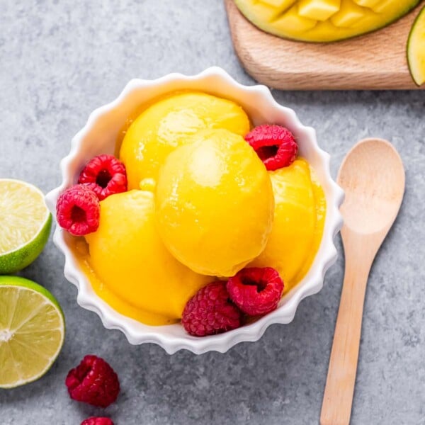 Mango sorbet in a bowl topped with raspberries.