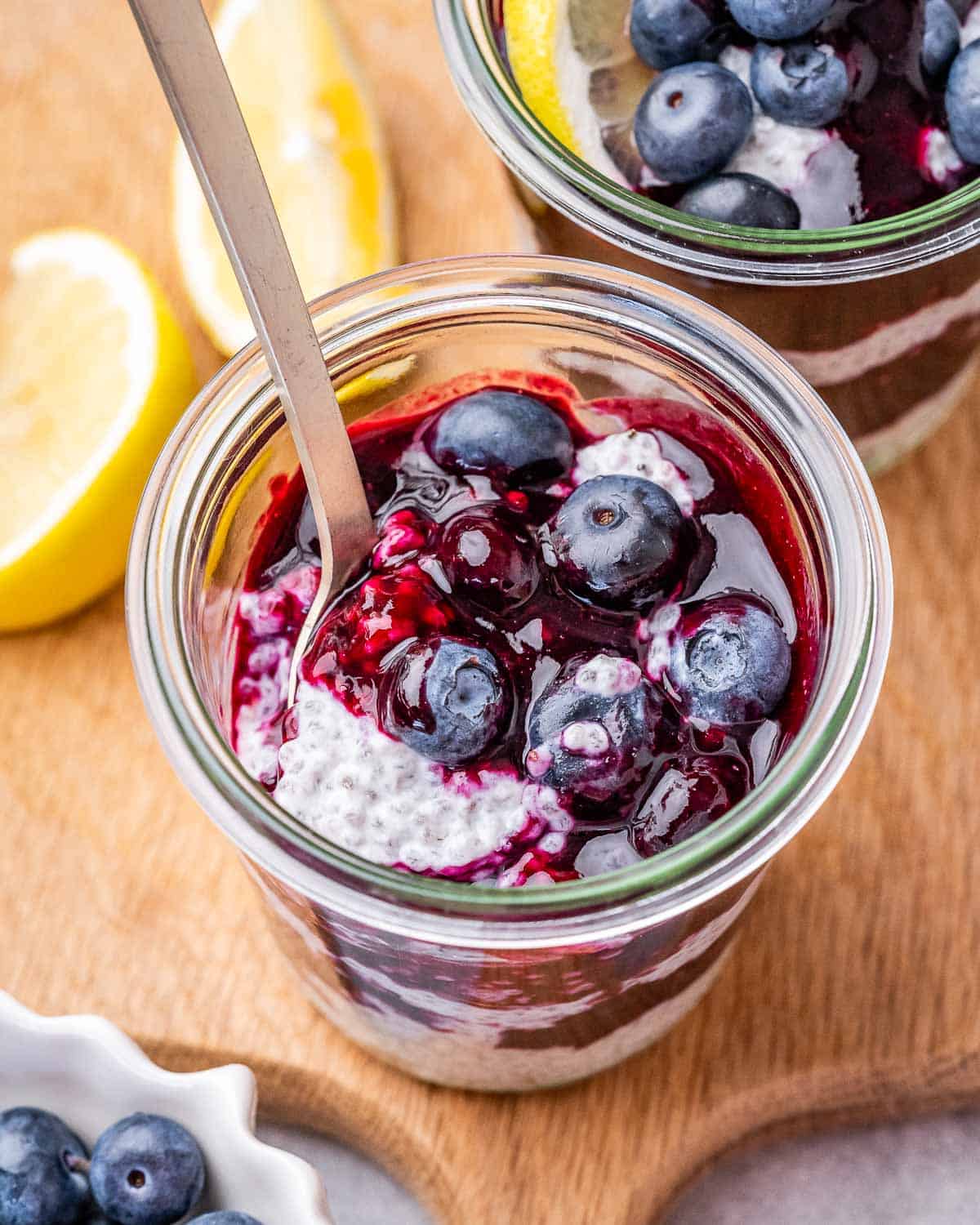 Spoon scooping blueberries from a chia pudding jar, with lemon slices in the background.