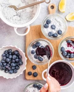 Ingredients spread out on a wooden board with bowls of blueberries and lemon chia pudding ready for layering.